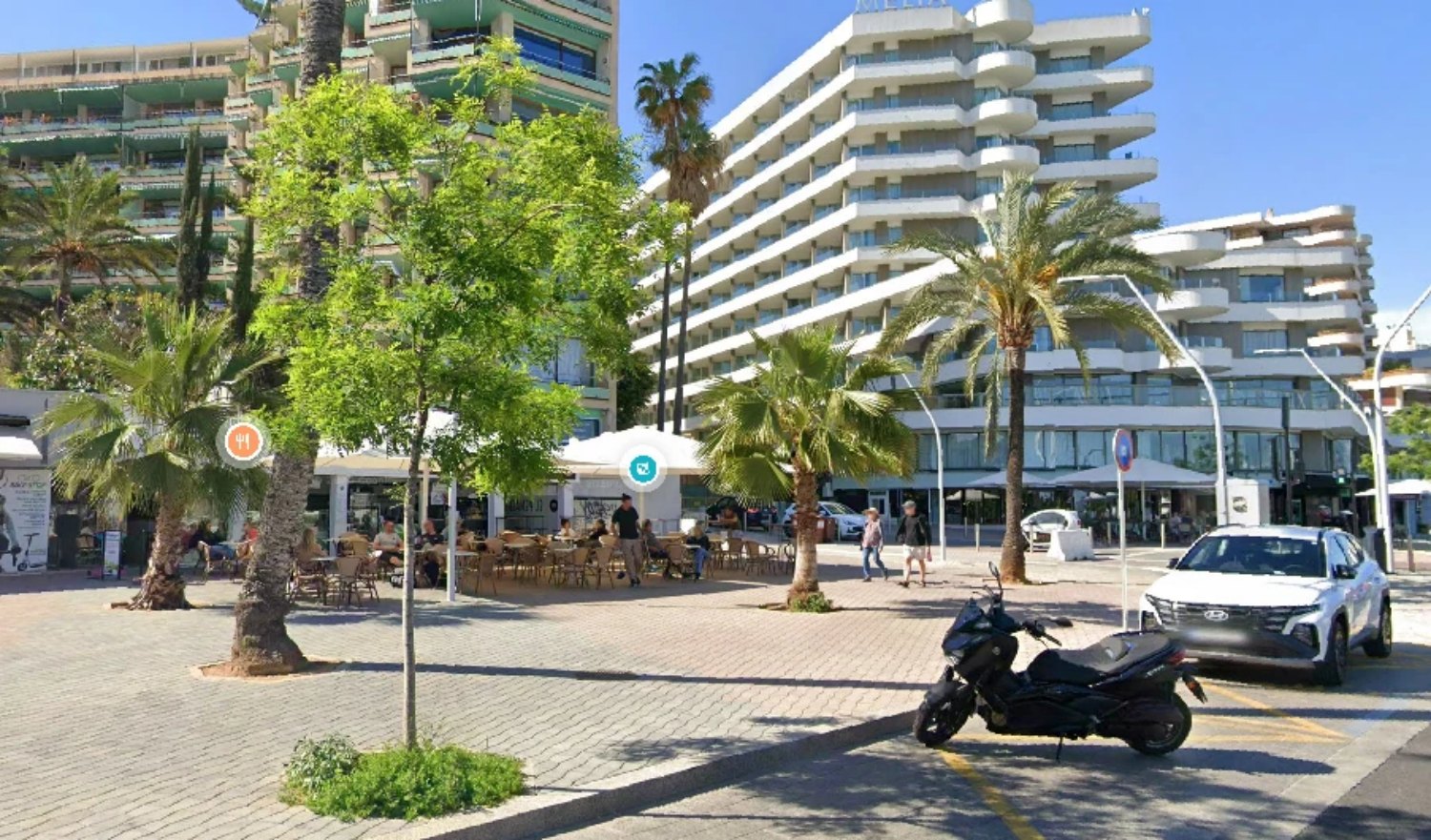 The frontage today: the plaza, the palms, the port at your feet